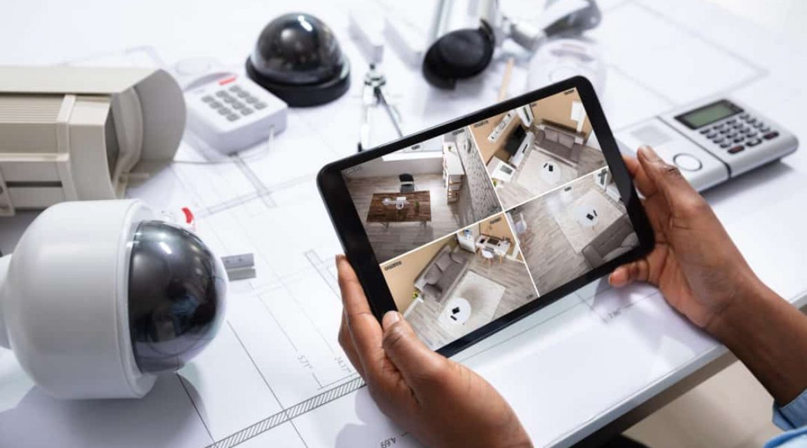 An Elevated View Of Person Watching Footage On Digital Tablet With Security Equipment On Blueprint